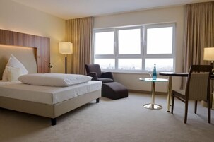 A hotel room with a bed, a chair, a small table, and a window with a view.