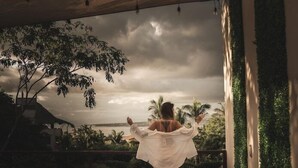 A person standing on a balcony with a view of palm trees and a cloudy sky. - Bora Boutique (Santa María Colotepec)
