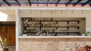 An outdoor dining area with wooden tables and chairs, a bar with shelves of bottles, and a ceiling fan. - Bora Boutique (Santa María Colotepec)