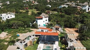 An aerial view of a resort with a swimming pool surrounded by lounge chairs and umbrellas, set against a backdrop of hills and scattered buildings. - Bora Boutique (Santa María Colotepec)