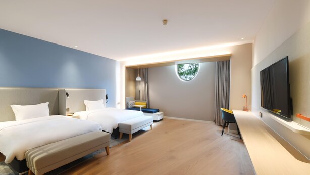 Ein Hotelzimmer mit zwei Betten, einem Schreibtisch, einem Fernseher und einem großen Fenster.
