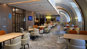A modern hotel lobby with a long corridor, seating areas, and a television screen.