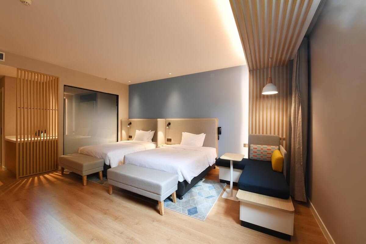 Una habitación de hotel moderna con dos camas, un escritorio, un banco y una mesita.