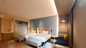 Ein modernes Hotelzimmer mit zwei Betten, einem Schreibtisch, einer Bank und einem kleinen Tisch.