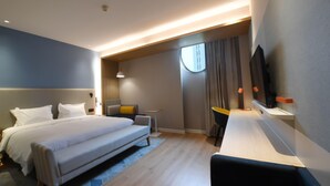 Ein modernes Hotelzimmer mit einem großen Bett, einem Schreibtisch, einem Sessel, einem Fernseher und einem Fenster mit Vorhängen.