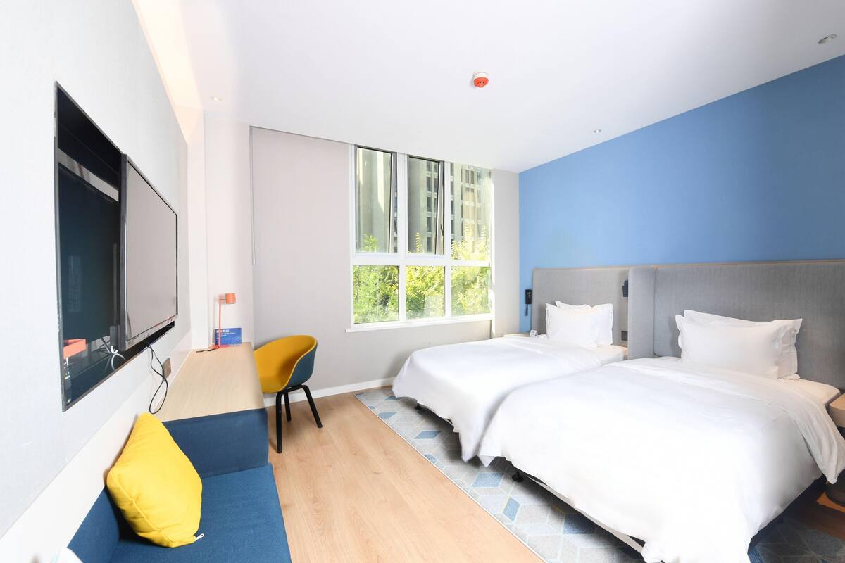 Una habitación de hotel con dos camas, un sofá, un televisor y un amplio ventanal.