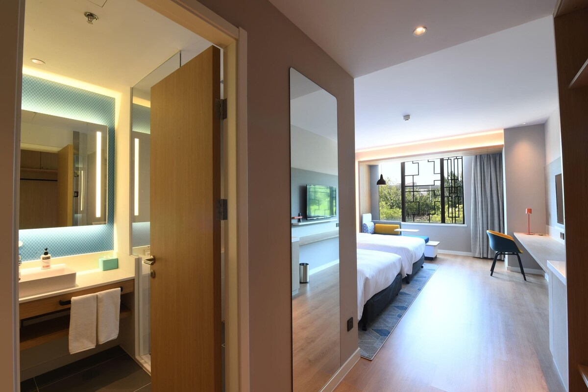 Ein Hotelzimmer mit Bad, Bett, Schreibtisch und einem großen Fenster.