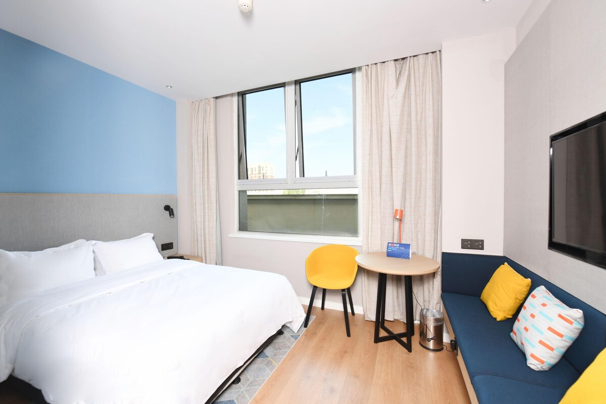 Ein Hotelzimmer mit einem Bett, einer Couch, einem kleinen Tisch, einem Sessel, einem Fernseher und einem Fenster mit Vorhängen.