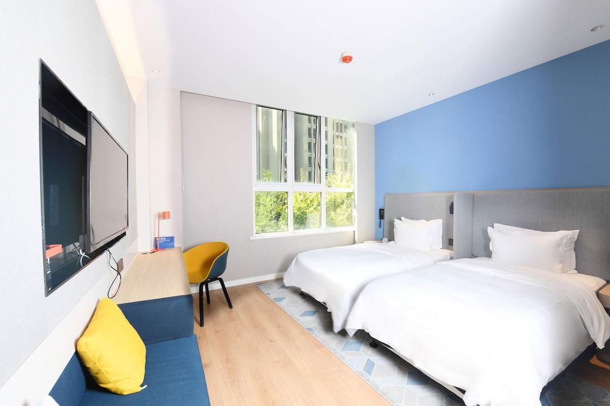Een hotelkamer met twee bedden, een bank, een televisie en een groot raam.