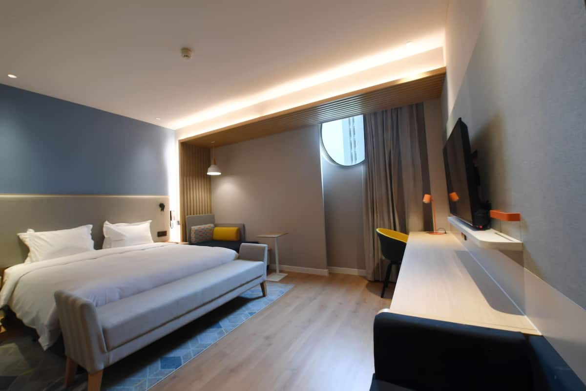 A modern hotel room with a large bed, a desk, a chair, a TV, and a window with curtains.