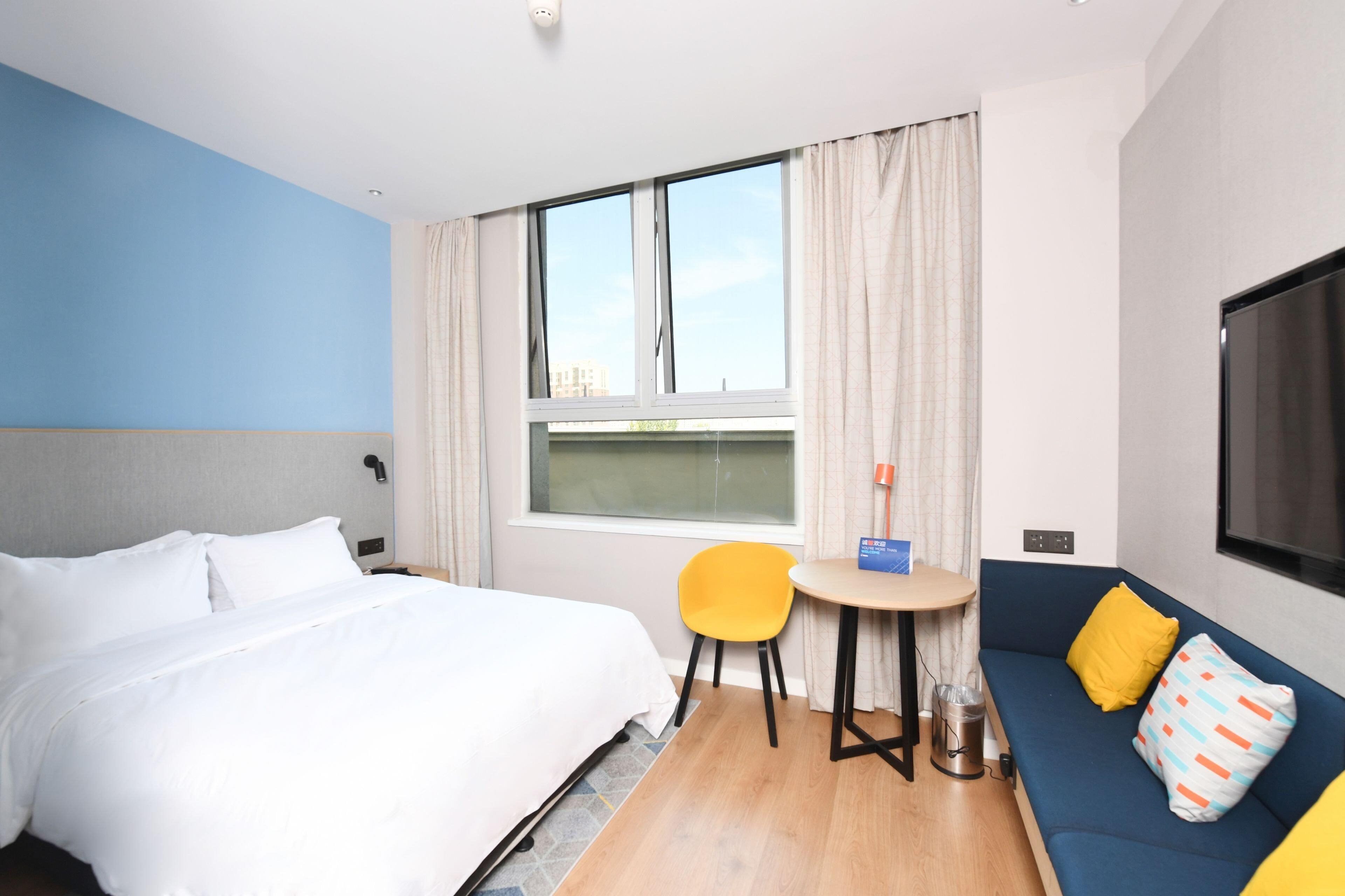 A hotel room with a bed, a sofa, a small table, a chair, a TV, and a window with curtains.
