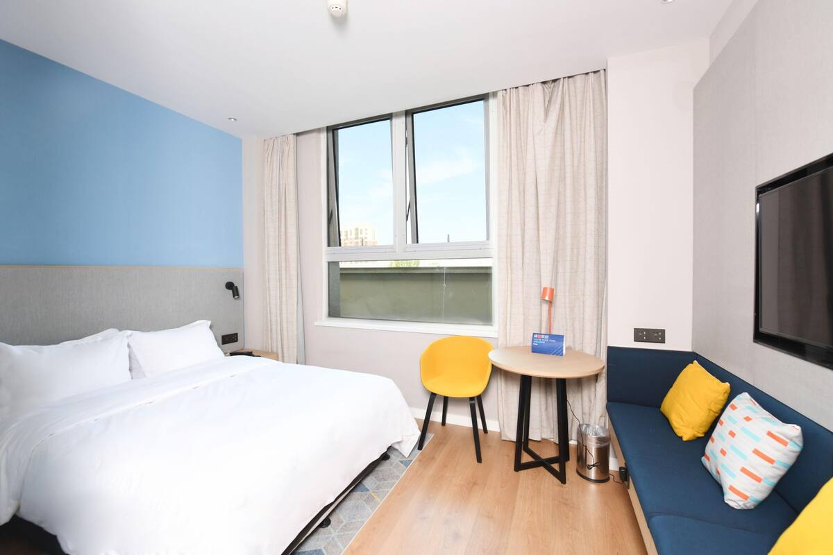 Una habitación de hotel con cama, sofá, una mesita, una silla, televisión y ventana con cortinas.