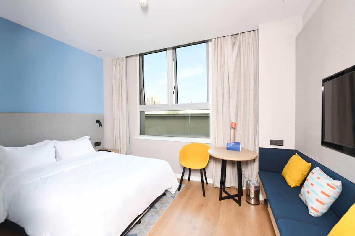 A hotel room with a bed, a sofa, a small table, a chair, a TV, and a window with curtains.