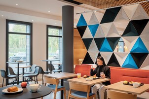 A modern cafe with tables and chairs, a large window, and a geometric wall design.
