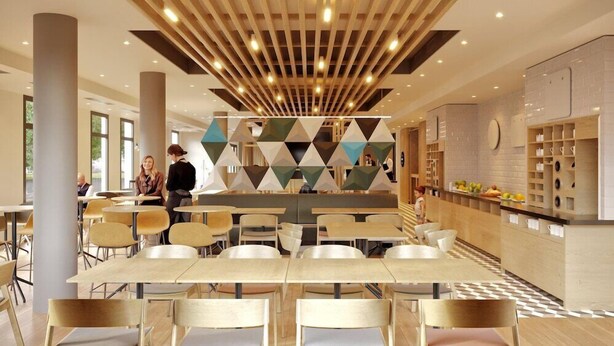 Un espace repas moderne avec des tables et des chaises hautes, un motif géométrique sur le mur et un coin cuisine avec des étagères.