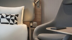 Une chambre d’hôtel moderne avec un lit, un fauteuil gris, une table de chevet avec un téléphone et une tablette.