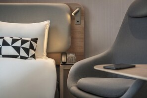 Une chambre d’hôtel moderne avec un lit, un fauteuil gris, une table de chevet avec un téléphone et une tablette.