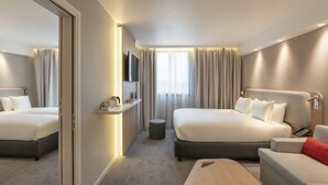 Une chambre d’hôtel moderne avec deux lits, un canapé, une petite table, une télévision et une fenêtre avec des rideaux.