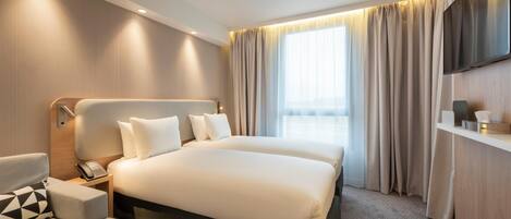 A hotel room with a large bed, a bedside table with a phone, a sofa, and a TV mounted on the wall.