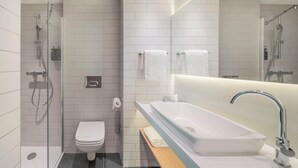 Une salle de bain moderne avec une douche à parois de verre, des toilettes blanches, un grand lavabo avec un robinet chromé et un miroir au-dessus du lavabo.
