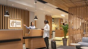 Un espace d’accueil d’un hôtel Holiday Inn Express, avec un lambris en bois, un comptoir d’accueil et un coin salon agrémenté d’une plante et d’une valise.