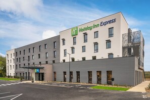 Un bâtiment de la chaîne Holiday Inn Express, doté d’un design moderne, avec un toit plat, de grandes fenêtres et une entrée bien visible.