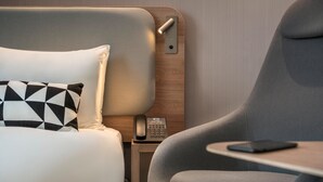 Une chambre d’hôtel moderne équipée d’un lit, d’une table de chevet avec un téléphone, d’une chaise et d’une petite table.