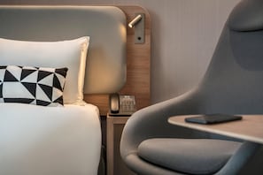 Une chambre d’hôtel moderne équipée d’un lit, d’une table de chevet avec un téléphone, d’une chaise et d’une petite table.