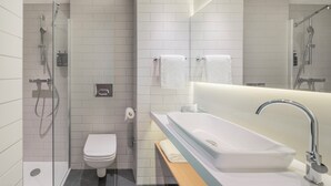 Une salle de bain moderne avec une douche à parois de verre, des toilettes blanches, un grand lavabo avec un miroir et un porte-serviettes.