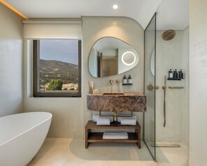 Un baño con una bañera grande, un lavabo de mármol, una ducha con cerramiento de vidrio y vistas a un paisaje montañoso a través de una ventana.