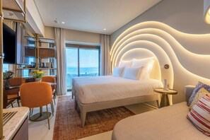 Un hotel moderno con una cama grande, un escritorio con silla, un televisor y vista al mar.