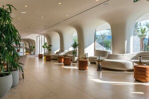 Eine großzügige Lobby im modernen Stil mit einer langen Sitzgruppe, Zimmerpflanzen und großen Fenstern mit Blick ins Freie.