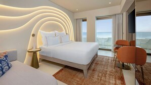 A modern hotel room with a large bed, a seating area with orange chairs, a TV, and a view of the sea. - Isla Brown Corinthia Resort & Spa, Curio Collection by Hilton (Loutraki-Agioi Theodoroi)