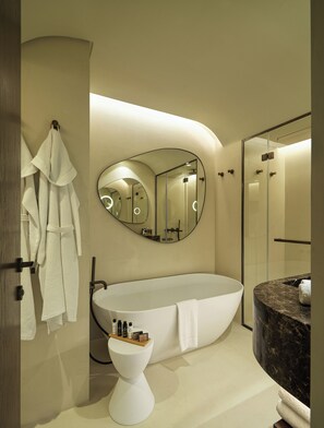 Un baño moderno con una bañera independiente, un espejo redondo y una ducha con mampara de vidrio.