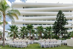 Un edificio moderno con varios balcones, rodeado de palmeras y mobiliario exterior.