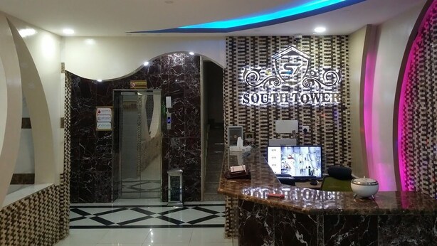 A hotel reception area with a marble reception desk, a digital screen displaying images, and a sign reading "SOUTH TOWER". - South Tower Hotel Apartment (Khamis Mushait)