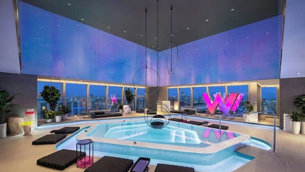 A modern indoor swimming pool with a city view, surrounded by lounge areas and large windows. - W Xiamen (Xiamen)
