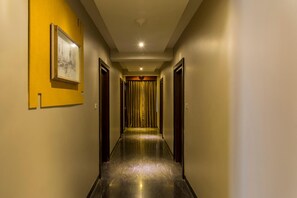 Un couloir d’hôtel avec un sol ciré, des portes en bois et un tableau encadré accroché au mur.