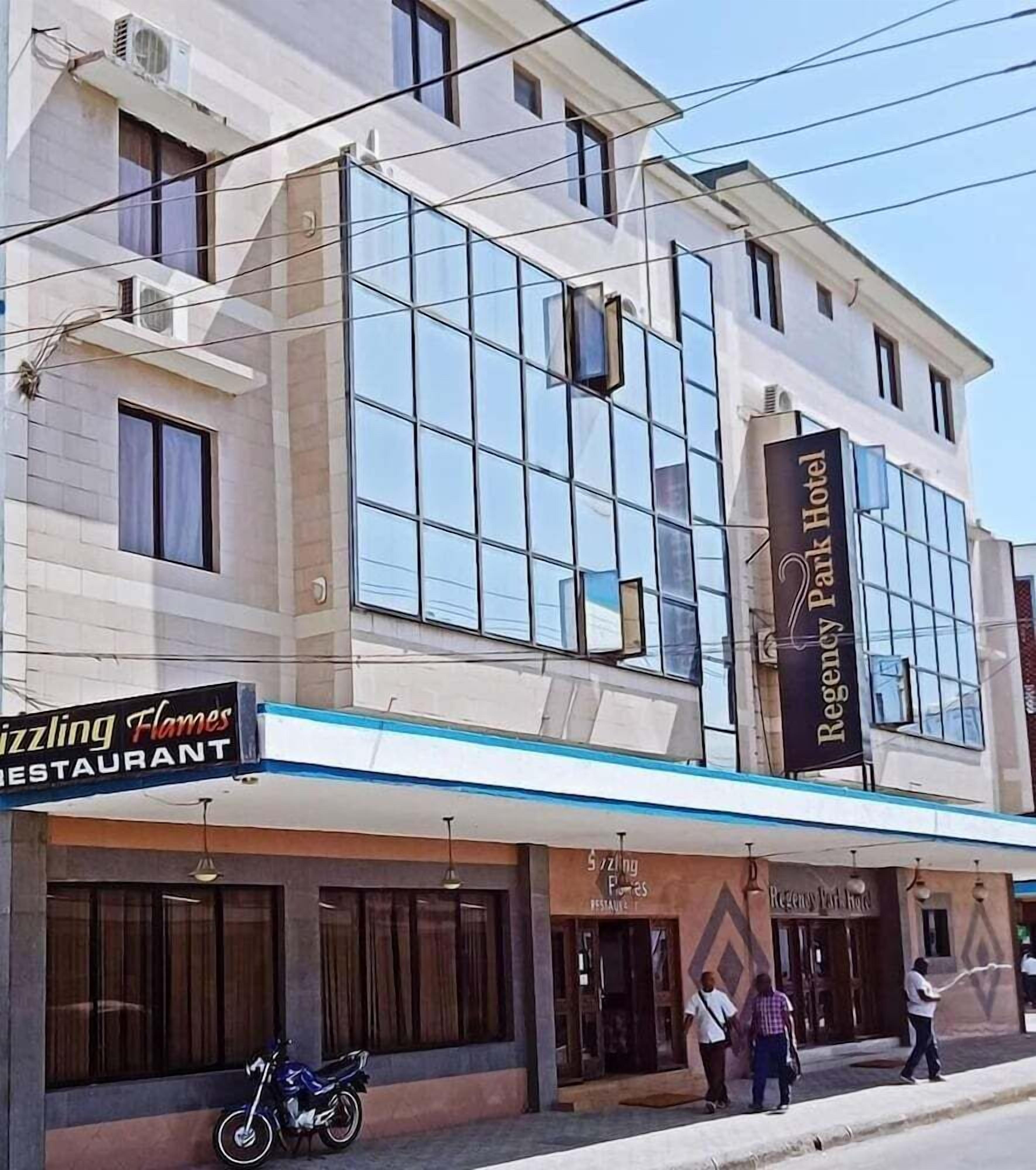 A building with a Regency Park Hotel sign, a restaurant named 'Zizzling Flames', and a motorcycle parked outside.