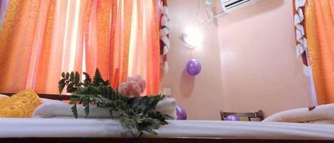 A hotel room with a bed, air conditioning unit, curtains, and a wall-mounted light fixture.