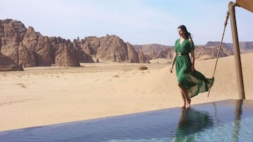 A desert landscape with a woman in a green dress standing by a pool.