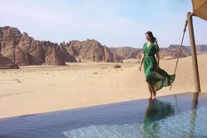 A desert landscape with a woman in a green dress standing by a pool.