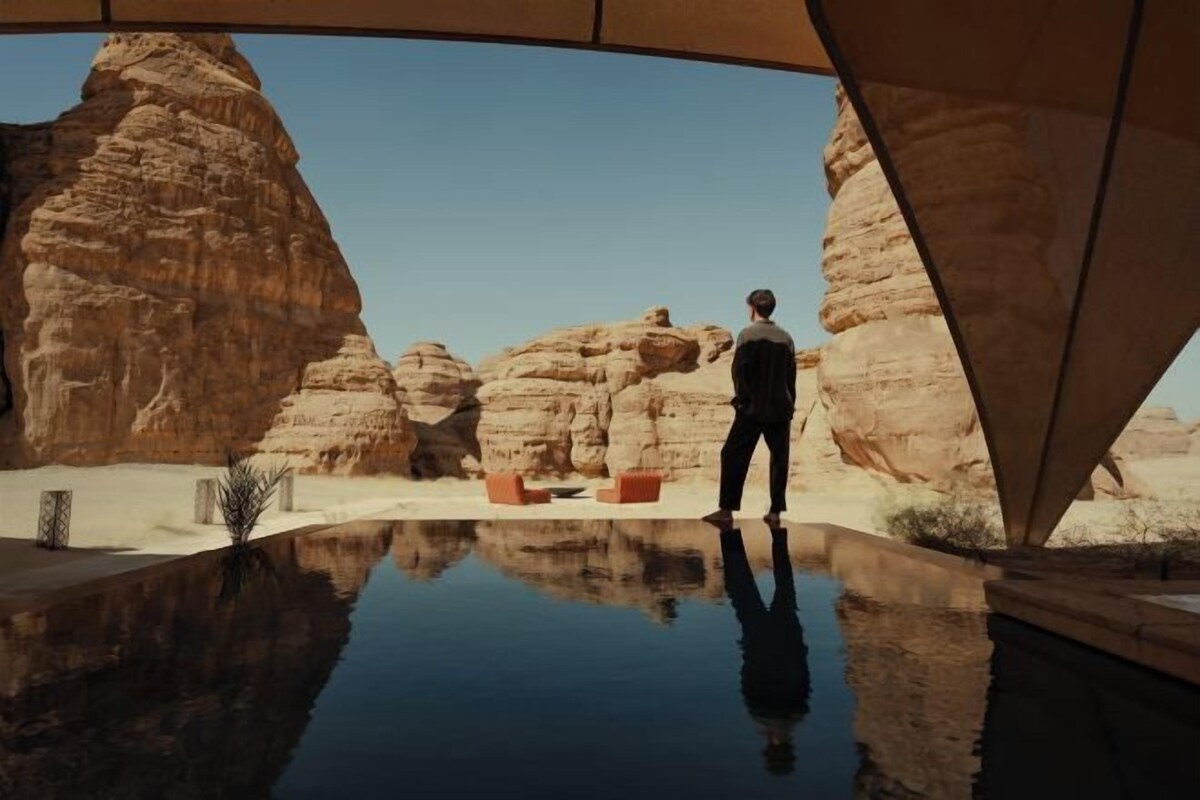 A man standing by a reflective pool with desert rock formations in the background.