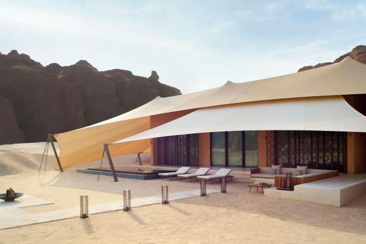 A modern building with a large overhanging structure, a pool, and outdoor seating.