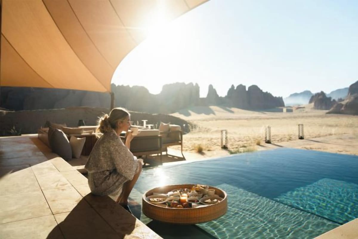 An outdoor pool area with a view of a desert landscape, a lounge chair, and a sunshade.
