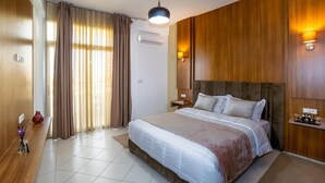 A hotel room with a large bed, wooden paneling, a bedside lamp, a small table, and a vase. - Sables D'or Appart & Hotel (Agadir)