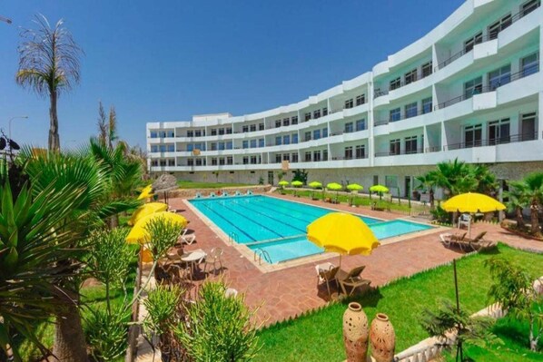 A hotel with a swimming pool, outdoor seating, and a well-maintained garden. - Sables D'or Appart & Hotel (Agadir)