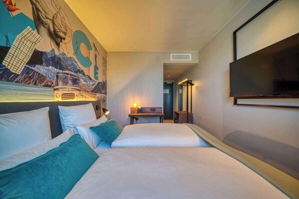 A hotel room with two beds, a mural on the wall, a television, and a desk with a lamp. - Nyce Hotel Ulm (Ulm)