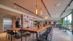 Ein modernes Restaurant mit einem langen Holztisch, schwarzen Stühlen und Pendelleuchten.