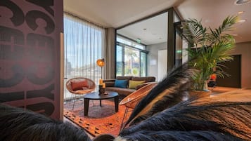 Un moderno vestíbulo de hotel con un ventanal grande, un sofá, sillas, una mesa de centro y una planta en maceta.